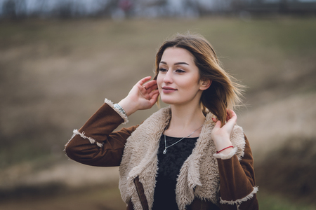 beautiful young women in field or track. girl in brown coat and black boots near the road. affective emotional spring portrait. lady with red manicure. sort straighten white short hair and smilingの写真素材