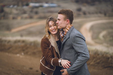 beautiful lovely couple in the park or field or track. man in coat and scarf with girl in coat. man hugs picked women up flirting laugh and look at each other. affective emotional soulful photoの写真素材