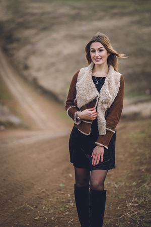 beautiful young women in the park or field or track. girl in brown coat and black boots near the road. affective emotional soulful spring portrait. lady with red manicure short white haircut smilingの写真素材