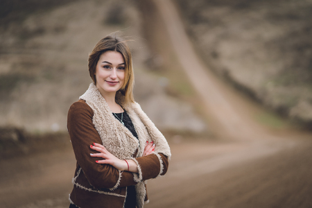 beautiful young women in the park or field or track. girl in brown coat near the road. emotional portrait. lady with red manicure short white haircut smiling. long road behind backgroundの写真素材