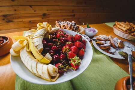 Big plate with a lot of delicious freshly banana cherries strawberries and sweets. Photo for restaurant or stand-up meal or banquet. healthy tasty food at the party. summer breakfast at the meatingの写真素材