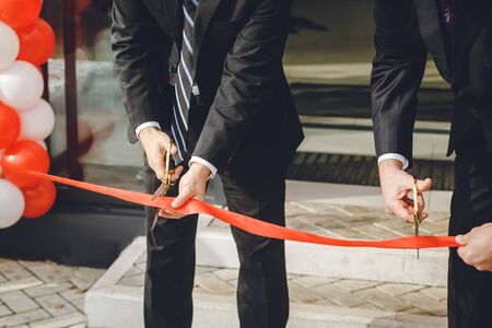 Businessman cutting red ribbon with pair of scissors. Two man in a classic black official suit cuts...