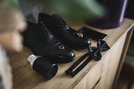 The groom is gathering in the morning. wooden shelf. Mens Black classic patent leather shoes. A black bow tie. Wedding details. Eau de toilette, black perfume, black mobile phoneの写真素材