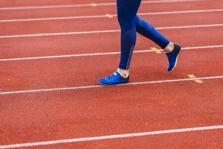Young fitness woman in blue shoes and blue leggings walking on running court or treadmill. Girl in blue sport wear close-up to shoes running court background. Health exercise life styleの写真素材