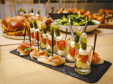 mini salads with tomato cheese and a sauce capsule in small glasses, ham greens, serving on a black clay tray plate. Real atmosphere of serving food in a restaurantの写真素材
