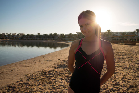 Sweet, slender girl stands on the beach against the sunset. The rays of the sun shine in the camera.の写真素材