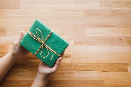 Green gift box on girl hand with wooden copy space background.Christmas new year and anniversary concepts ideasの写真素材