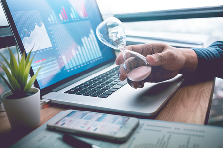 Business concepts with businessman holding hourglass with graph chart on computer laptop.For...