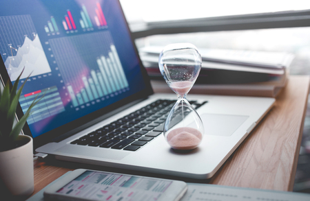Business concepts with businessman holding hourglass with graph chart on computer laptop.For...