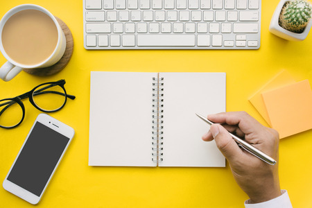 Top view of office desk table with male hand on notepad and modern accessories.flat lay design.business concepts ideasの写真素材