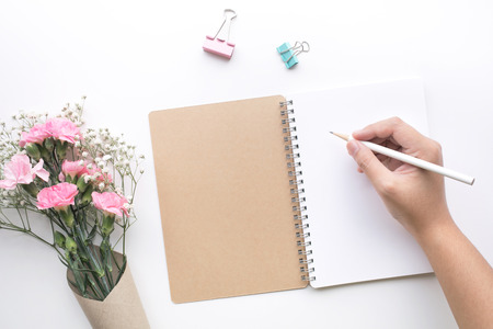 Home office desk table with woman hand,notepad,flower on white background.Flat lay.feminine concepts design.minimalist styleの写真素材