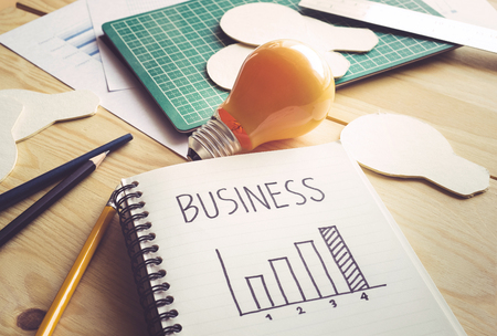 Business graph on notebook with lightbulb on wooden table.Ideas,creativity,education,inspiration and start up concepts.の写真素材