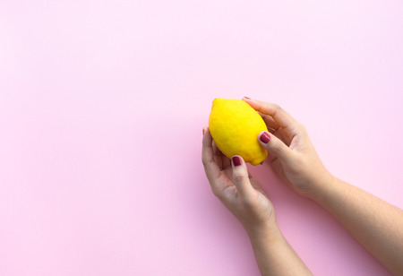 Young female hand holding lemon on pink pastel background.fruit and healthy concepts ideasの写真素材