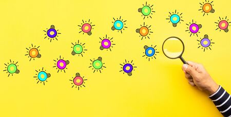 Ideas inspiration concepts with hand using magnifying glass looking for group of lightbulb on pastel color background.Business creativity.human performanceの写真素材