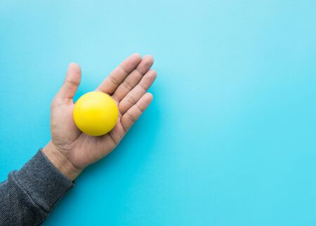 Male hand holding yellow ball on blue color background