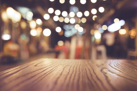 Wood table top with blur of lighting in night cafe restaurant (community) background/selective focus.の写真素材