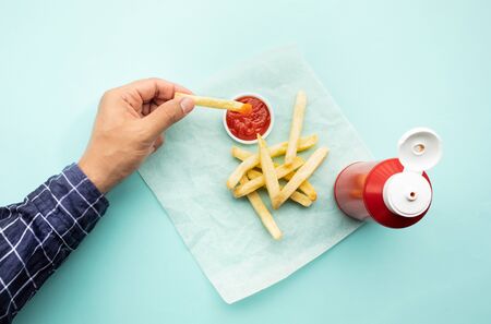 Top view of youngman enjoy eating with french fried and dipping  tomato sauce ( ketchup ) on color table background.Fast food and healthy concepts ideasの写真素材