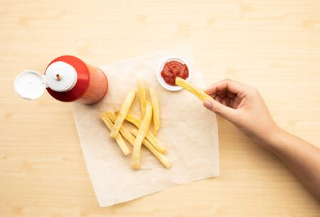 Top view of youngwoman dipping french fried  with tomato sauce ( ketchup ) on wood table background.Fast food and healthy concepts ideasの写真素材