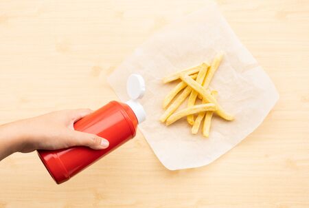 Top view of youngwoman squeezing a bottle sauce ( ketchup ) for dipping with french fried on wood table background.Fast food and healthy concepts ideasの写真素材