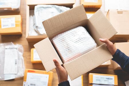 Online shopping concepts with male hand packing some product to brown box on another packet for...