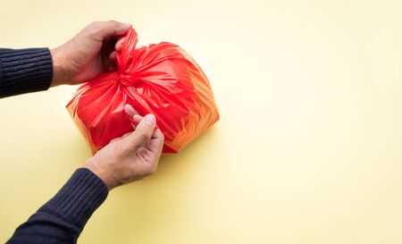 Male hand packing food trash with red plastic bag on color background.Recycle and environment concepts ideasの写真素材