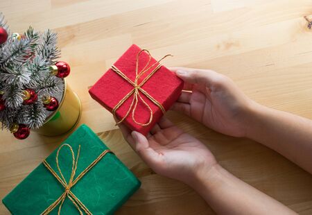 Merry christmas concepts with female hand holding gift box present and ornament element on wood table background.winter season's greeting ideas.top viewの写真素材
