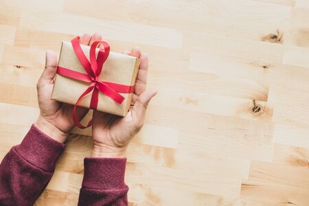 Gold gift box on male hand on wooden table background.Christmas new year and anniversary concepts...