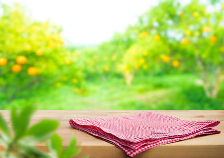 Red checked cloth on wood table top with blur of orange garden farm background.For montage product display or design key visual layoutの写真素材