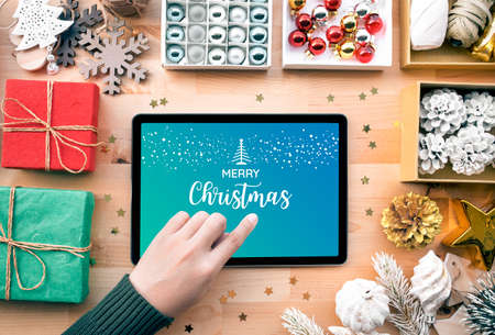 Young female using tablet with merry christmas text sign on screen and ornament element for decorating on wood table.digital marketing,online businessの写真素材