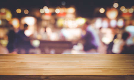 Selective focus.Wood table top with blur light bokeh in dark night cafe,restaurant...