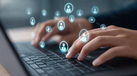 Close-up image of hands typing on a laptop keyboard, with digital icons floating above, depicting connectivity and digital communication in a modern workspace setting.の素材