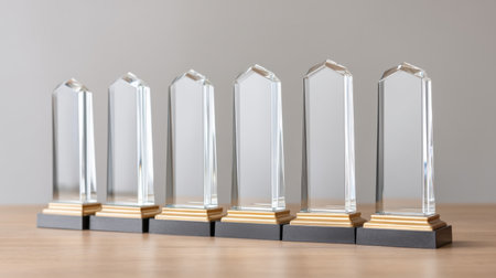 A series of empty glass awards positioned on a wooden table, perfect for showcasing excellence and celebrating achievements in various fields and industries.の素材