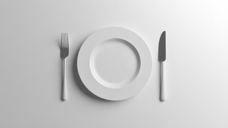 An aesthetically arranged dining setting featuring a white plate, fork, and knife on a clean white background, evoking elegance.の素材