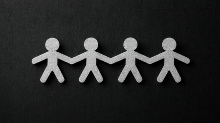 This image features paper cutouts of human figures holding hands against a textured black surface, representing themes of unity, connection, and community in a clean, minimalist style.の素材