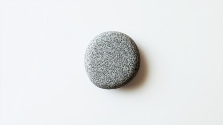 Minimalist image of a round gray pebblestone isolated on a clean white background, focusing on simplicity and natural formの素材
