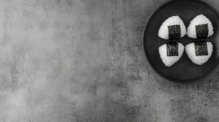 A plate of traditional onigiri, rice balls wrapped in nori, neatly arranged on a simple, clean background.の素材