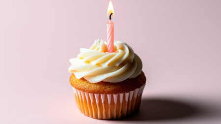 A small, beautiful cupcake with a lit candle on top, set against a pale pink background, perfect for a simple and elegant birthday celebration.の素材