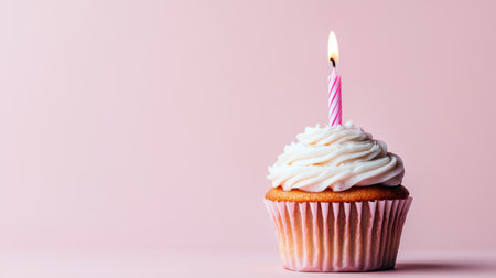 Beautiful cupcake with a single candle on a pale pink background, representing a soft and sweet birthday moment.の素材