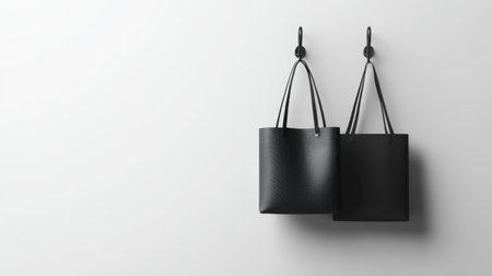 Two stylish black bags hang elegantly on hooks against a subtle background, showcasing a minimalist design perfect for any modern space or decor style.の素材