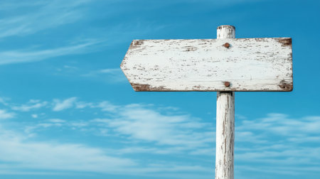 Rustic white wooden signpost with weathered texture against a vibrant blue sky, evoking a vintage guidance concept in a rural setting.の素材