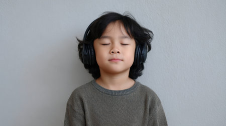 A young child in a cozy setting enjoys music through headphones with a peaceful expression. The closed eyes capture a moment of joy and relaxation through sound.の素材