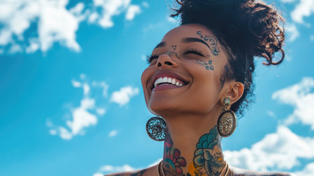 Ethnic woman with tattoos and piercings, smiling peacefully in nature, a blue sky backdrop highlighting her joy.の素材
