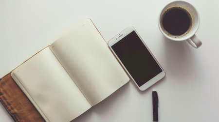 Flat lay of an open notebook with a smartphone and coffee cup, on a white tableの素材