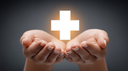 A pair of hands gently cradling a glowing healthcare cross icon, symbolizing healing and support. This image represents compassion and wellness in the healthcare field.の素材