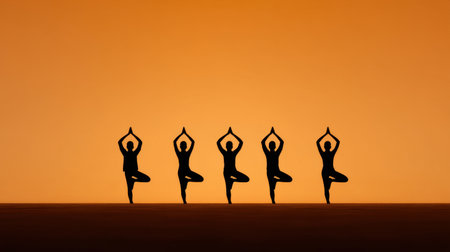 A serene group of silhouetted individuals practicing yoga at dusk against a tranquil orange sky, promoting peace and mindfulness in a natural setting.の素材
