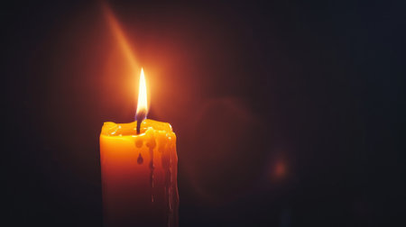 A single illuminated candle flickering against a velvety black background, casting a warm glow.の素材