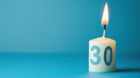 A lit white candle featuring the number thirty stands out against a calming blue background, symbolizing celebration and joy for a milestone birthday event.の素材