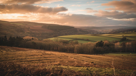 A serene sunset over a landscape of rolling hills and fields in shades of brown and greenの素材