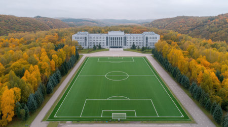 This aerial image captures a vibrant soccer field nestled among autumn trees, with a modern building in the background, creating a picturesque outdoor sports setting.の素材
