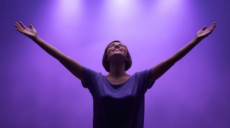 A joyful woman stands with arms raised in a powerful pose under enchanting purple lights, showcasing freedom and positivity in a serene and uplifting environment.の素材